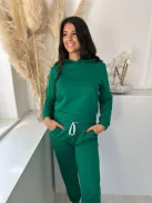 Rugalmas anyagú melegítő szett. Zsebes, kapucnis, rövid derekú felsőrész, gumis, magas derekú, zsebes nadrággal. A Modell S/M méretet visel. (S/M és L/XL méretekben.)